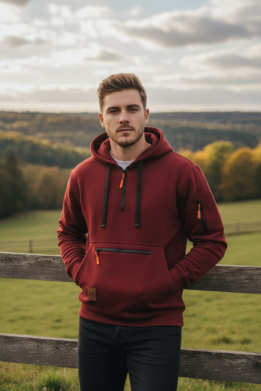 A dark red pullover hoodie with black drawstrings, a black horizontal chest zipper, and orange zipper pulls, shown on a plain white background.