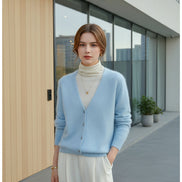 A person wearing a light blue fuzzy V-neck cardigan over a cream turtleneck, with cream trousers 