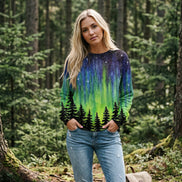 A woman wearing a long-sleeve crewneck sweatshirt with a vibrant aurora borealis print. The design features a dark starry sky at the top, transitioning into bright green 