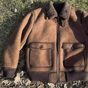 A brown suede aviator-style jacket with a dark brown shearling collar, laid flat on grass with dry leaves.