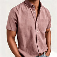 A man wearing a dusty rose short-sleeve button-up shirt with a chest pocket, paired with blue jeans and a brown leather belt, 