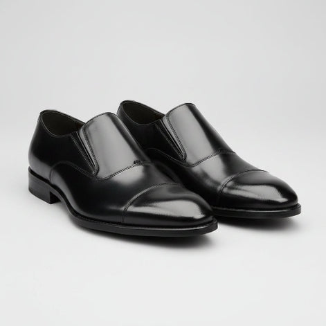 Black dress shoes worn with black pants on a gray background