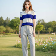 A woman wearing a short-sleeve collared knit top with bold horizontal stripes in royal blue and off-white, seated in a brown leather chair.