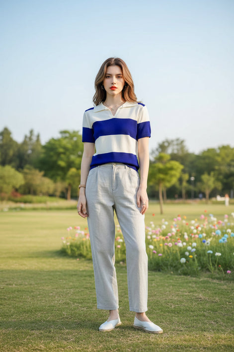 A woman wearing a short-sleeve collared knit top with bold horizontal stripes in royal blue and off-white, seated in a brown leather chair.