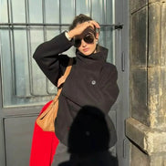 Woman wearing a black stand-collar short coat with a tan shoulder bag in sunlight