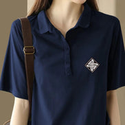 A navy blue short-sleeve polo shirt with a small white geometric emblem on the left chest, shown on a model wearing a brown shoulder bag.