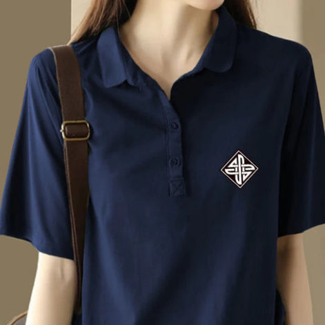 A navy blue short-sleeve polo shirt with a small white geometric emblem on the left chest, shown on a model wearing a brown shoulder bag.