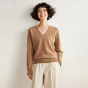 Woman wearing a brown sweater and white pants against a plain background