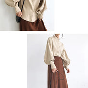 Person wearing a beige blouse and brown skirt with a black handbag against a white background