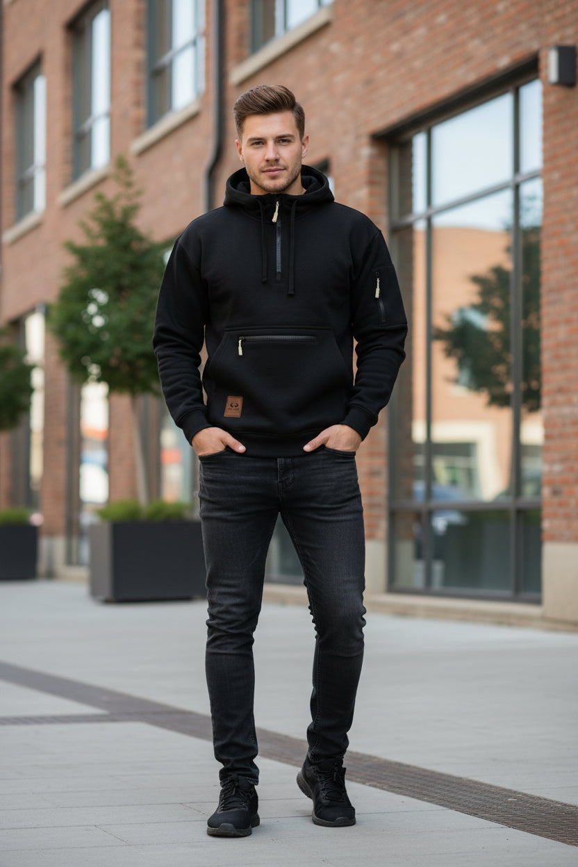 A black pullover hoodie with a half-zip neckline, a front kangaroo pocket with a horizontal zip, a sleeve zip pocket, and a brown brand patch on the lower left front.