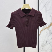 A short-sleeve ribbed knit polo shirt in deep plum purple, hanging on a light wood hanger against a split textured wall background.