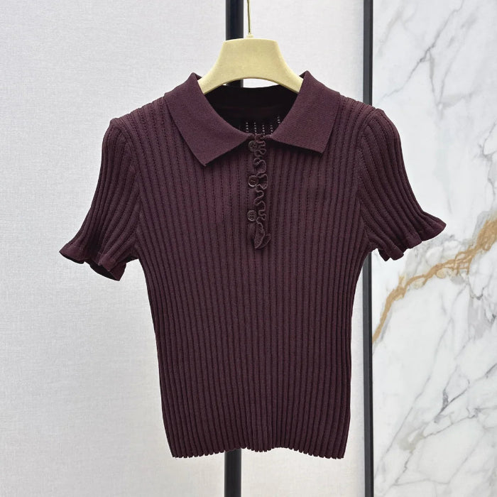 A short-sleeve ribbed knit polo shirt in deep plum purple, hanging on a light wood hanger against a split textured wall background.