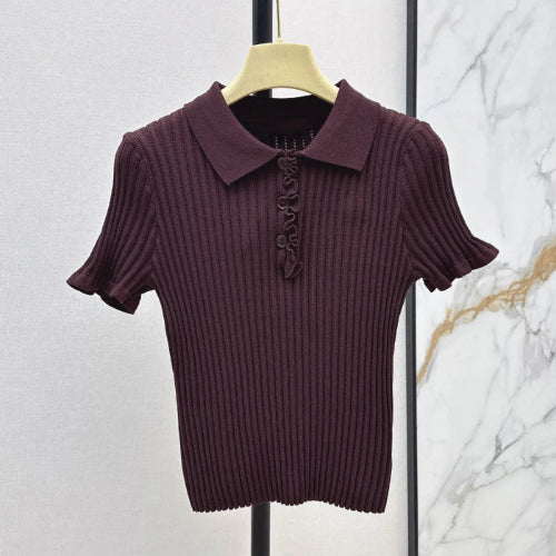 A short-sleeve ribbed knit polo shirt in deep plum purple, hanging on a light wood hanger against a split textured wall background.