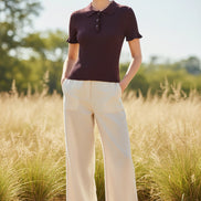 A short-sleeve ribbed knit polo shirt in deep plum purple, hanging on a light wood hanger against a split textured wall background.