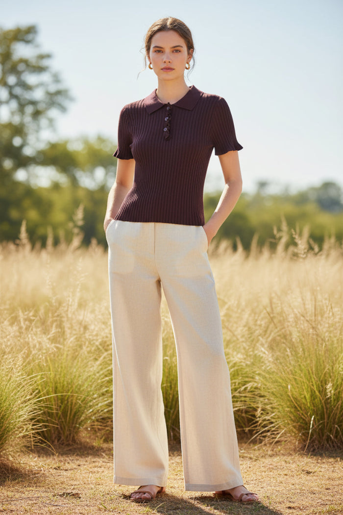 A short-sleeve ribbed knit polo shirt in deep plum purple, hanging on a light wood hanger against a split textured wall background.
