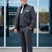 Man wearing a gray suit with a vest and tie, standing in front of a glass door.