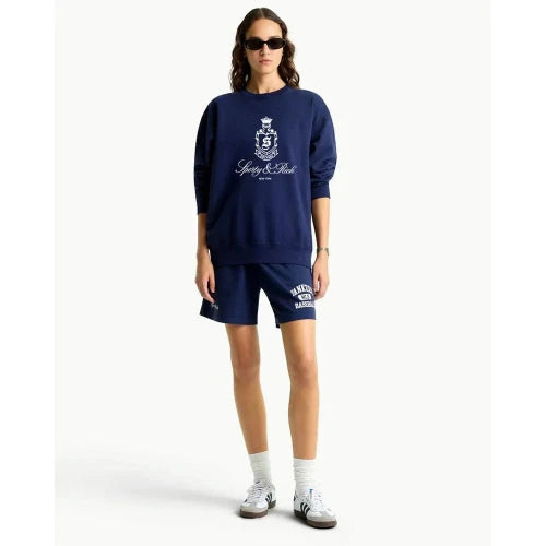 Person wearing navy blue sweatshirt and shorts with a logo, standing against a white background