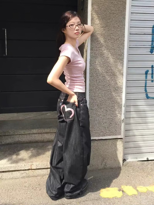 Woman posing sideways in dark-wash loose-fit jeans with contrast stitching, her hand in the back pocket featuring a pink heart outline.