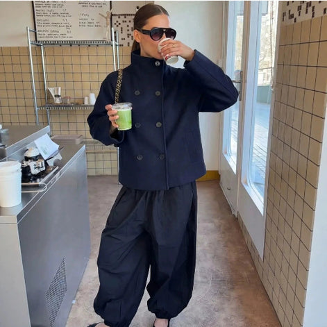 Woman wearing a navy double-breasted short coat with black trousers in a café