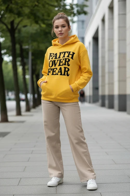 Yellow hoodie with 'Faith Over Fear' text on a light gray surface.