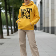 Yellow hoodie with 'Faith Over Fear' text on a light gray surface.