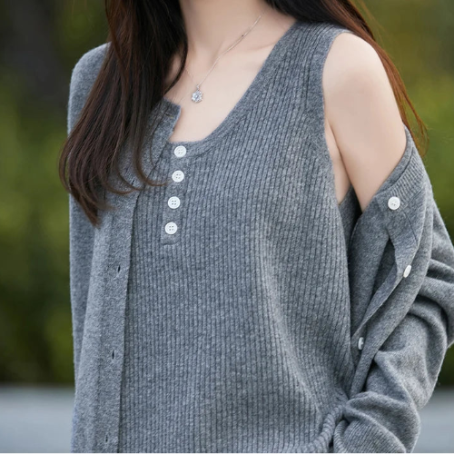 A woman wearing a gray ribbed knit cardigan with a V-neck, button placket, and cold-shoulder cutout detail, photographed outdoors with a blurred green background.