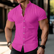 A muscular man wearing a bright pink short-sleeve button-up shirt with a textured grid pattern, shown from the chest down in an outdoor urban setting.
