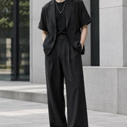 A men's two-piece outfit consisting of a black short-sleeve blazer layered over a black t-shirt and paired with black wide-leg trousers, 