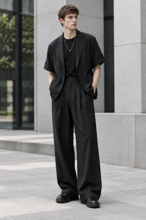 A men's two-piece outfit consisting of a black short-sleeve blazer layered over a black t-shirt and paired with black wide-leg trousers, 