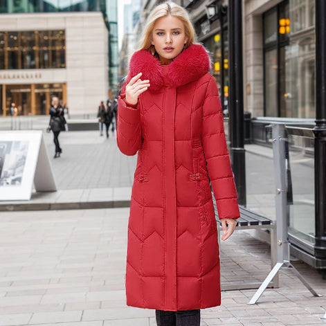 A woman wearing a long red puffer coat with a large fluffy faux-fur collar stands on a city sidewalk. The coat has horizontal quilting and a high collar.