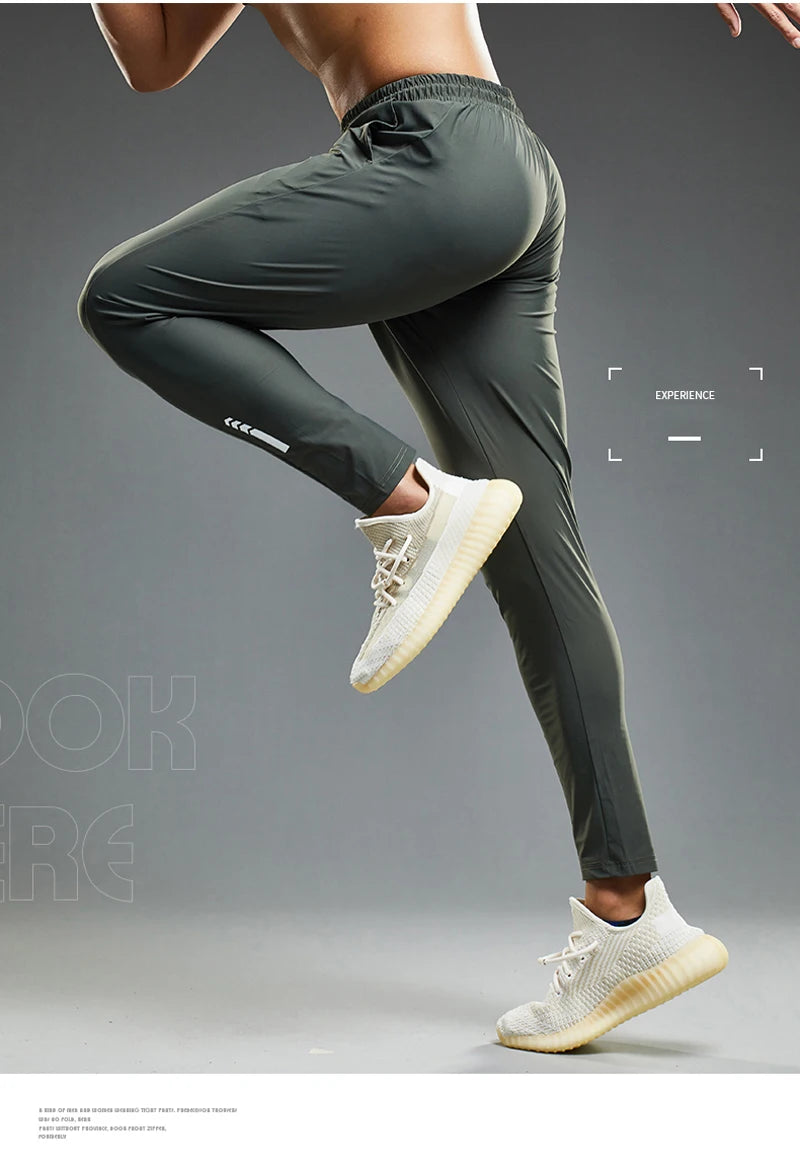 Person wearing dark gray athletic pants and white sneakers on a gray background