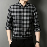 A man wearing a black and white plaid long-sleeve button-up shirt, paired with black trousers and a black belt,