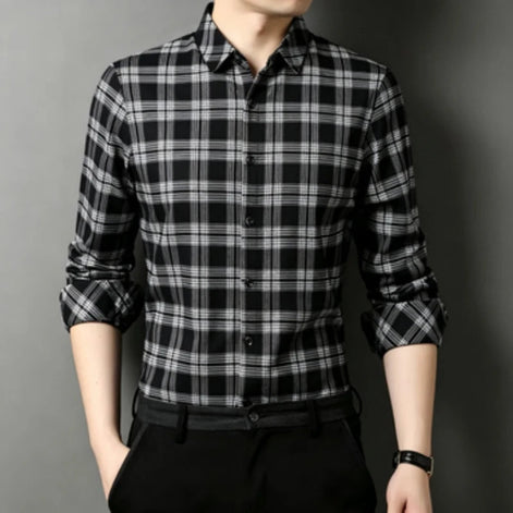 A man wearing a black and white plaid long-sleeve button-up shirt, paired with black trousers and a black belt,