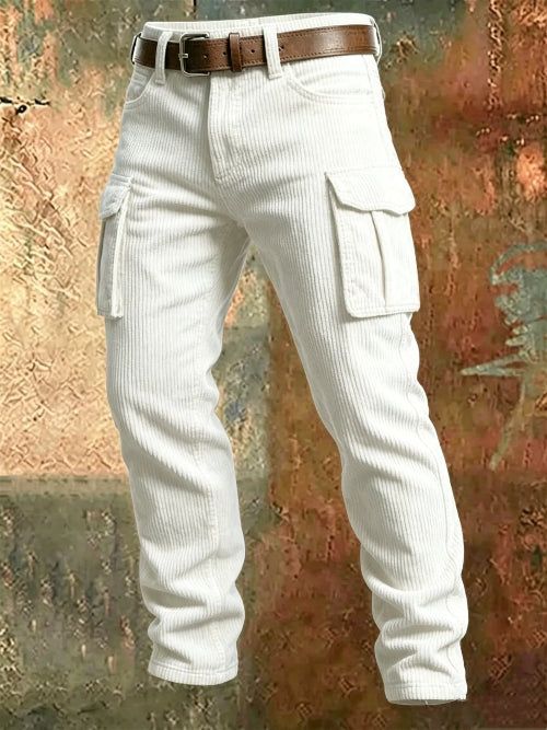 White corduroy cargo pants with flap thigh pockets and a brown belt against a textured rust-colored metal background.