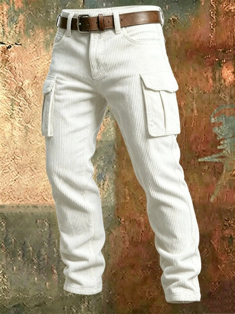 White corduroy cargo pants with flap thigh pockets and a brown belt against a textured rust-colored metal background.