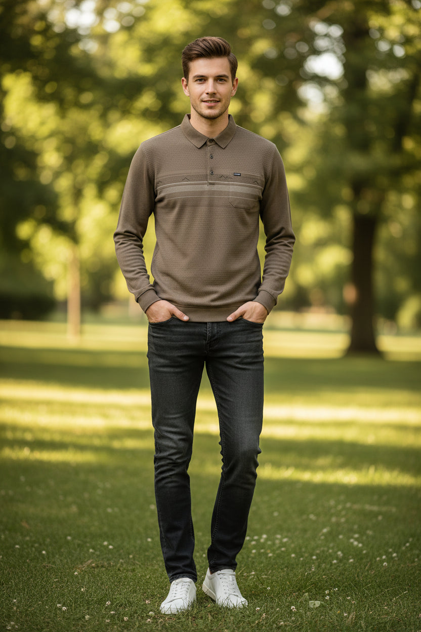 A taupe-brown long-sleeve polo shirt with a textured knit pattern, featuring a collar, three-button placket, and a chest pocket with decorative mountain line embroidery. An inset image in the top right shows a sheep with text reading 'INCLUDES WOOL', 'SKIN FABRIC', and 'SOFT'.