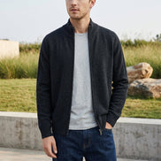 A dark charcoal gray knit zip-up sweater with a mock neck collar, hanging on a wooden hanger against a light gray background. 