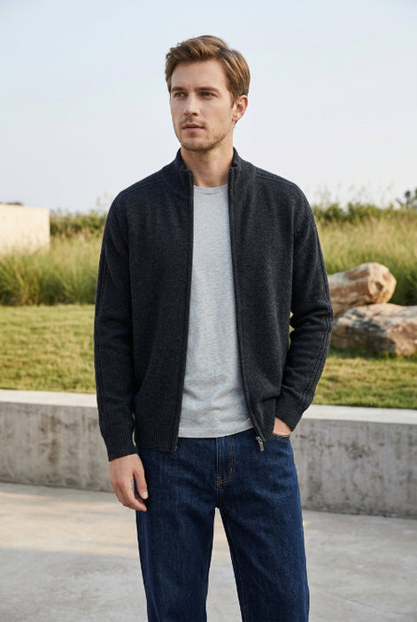 A dark charcoal gray knit zip-up sweater with a mock neck collar, hanging on a wooden hanger against a light gray background. 