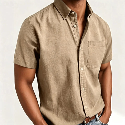 A man wearing a short-sleeve button-up shirt in a light tan or khaki color, paired with blue jeans and a brown leather belt, 