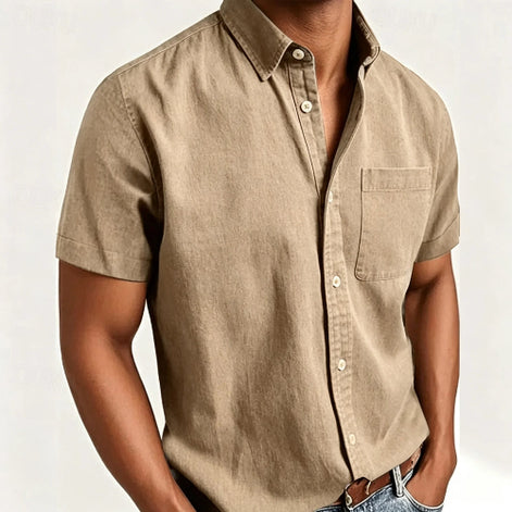 A man wearing a short-sleeve button-up shirt in a light tan or khaki color, paired with blue jeans and a brown leather belt, 