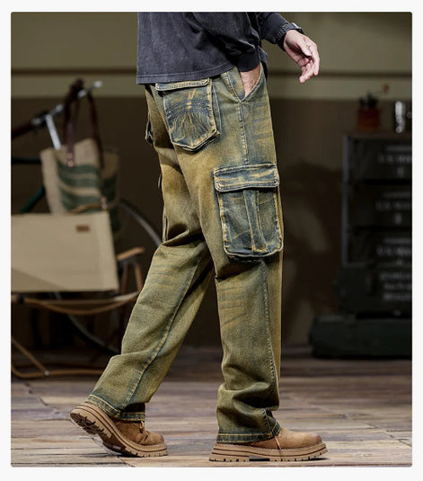 Rear-side view of a model wearing faded olive-brown cargo pants with a large flap thigh pocket and decorative stitching on a back pocket, paired with brown boots.⠋
