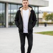 Black hoodie with beige lining on a hanger against a tiled wall background