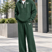 A person wearing a dark green waffle-knit hoodie and matching sweatpants set with small white Reebok logos, shown 