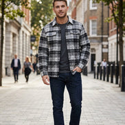 A long-sleeve plaid button-up shirt laid flat on a textured gray surface, with a black fleece lining visible at the open bottom front.