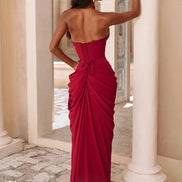 A woman wearing a strapless deep red evening gown with a structured corset-style bodice and dramatic draped skirt,