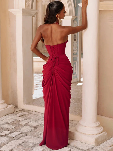 A woman wearing a strapless deep red evening gown with a structured corset-style bodice and dramatic draped skirt,