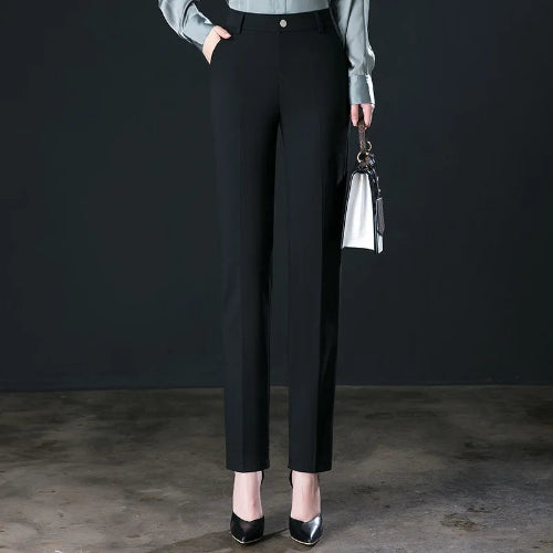 Person wearing black pants and holding a handbag against a dark background