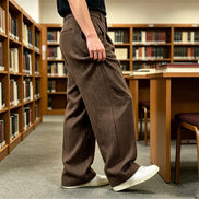 Brown herringbone wide-leg pants worn by a man walking in a library