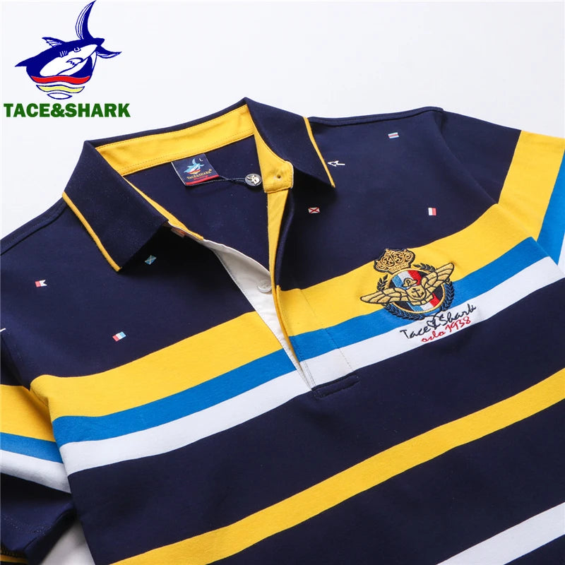 A close-up of a Tace&Shark rugby-style polo shirt with horizontal navy, yellow, blue, and white stripes, featuring a printed eagle crest on the chest and the Tace&Shark logo in the top-left corner.