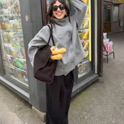 Woman wearing a gray double-breasted short coat with black wide-leg trousers outside a shop
